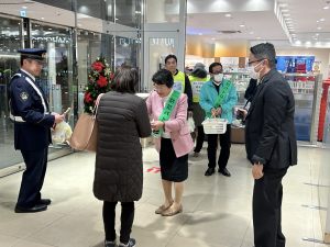 東武百貨店入口にてみどりのタスキをかけ防犯の啓発グッツを配りながら声掛け