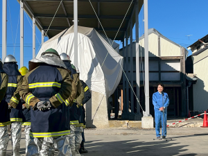 消防団員のまえで青い防災服を着て挨拶