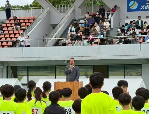 大勢の黄色いTシャツを着た選手の前で開会式のご挨拶
