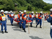 消防団が救命ボートを持ち水の中前進する訓練